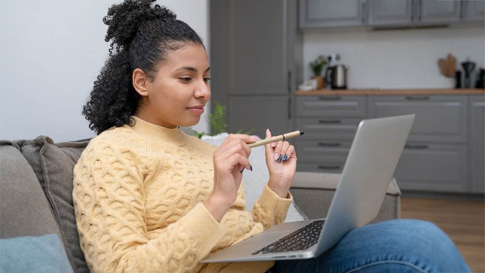 Mulher empreendedora sentada no sofá com notebook no colo, criando conteúdo para o seu negócio