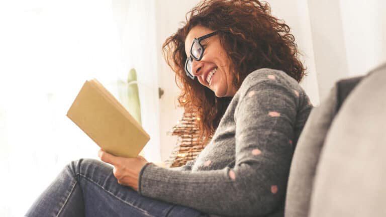 Mulher sorridente lendo um livro em casa, representando o poder da leitura e o incentivo aos livros para mulheres empreendedoras.
