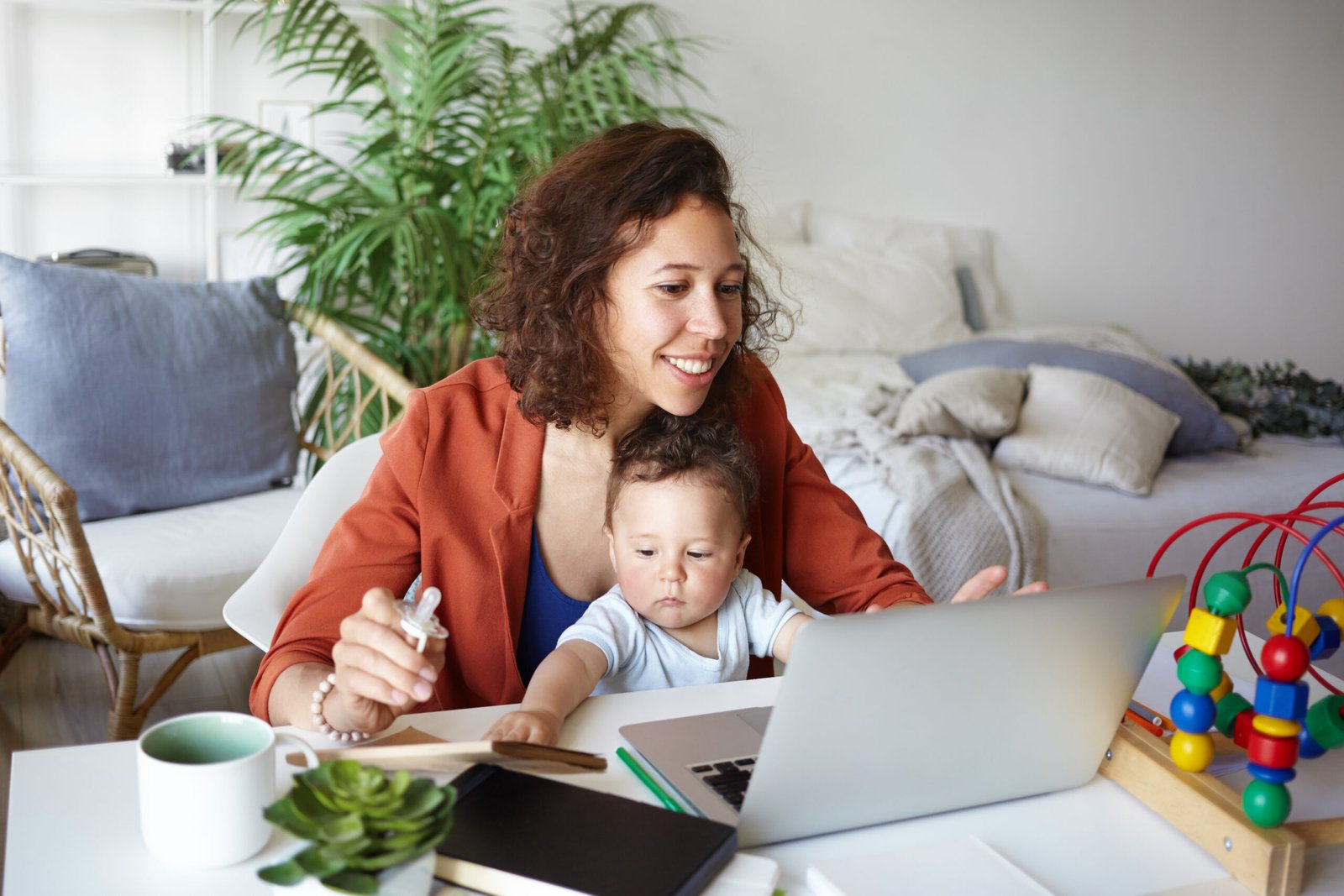 Mulher trabalhando em um notebook com um bebê no colo dentro de casa, ilustrando a realidade de negócios e maternidade. A imagem representa o empreendedorismo materno, a busca por equilíbrio entre carreira e família e a criação de negócios inspirados pela maternidade.